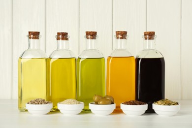 Vegetable fats. Different cooking oils in glass bottles and ingredients on white wooden table