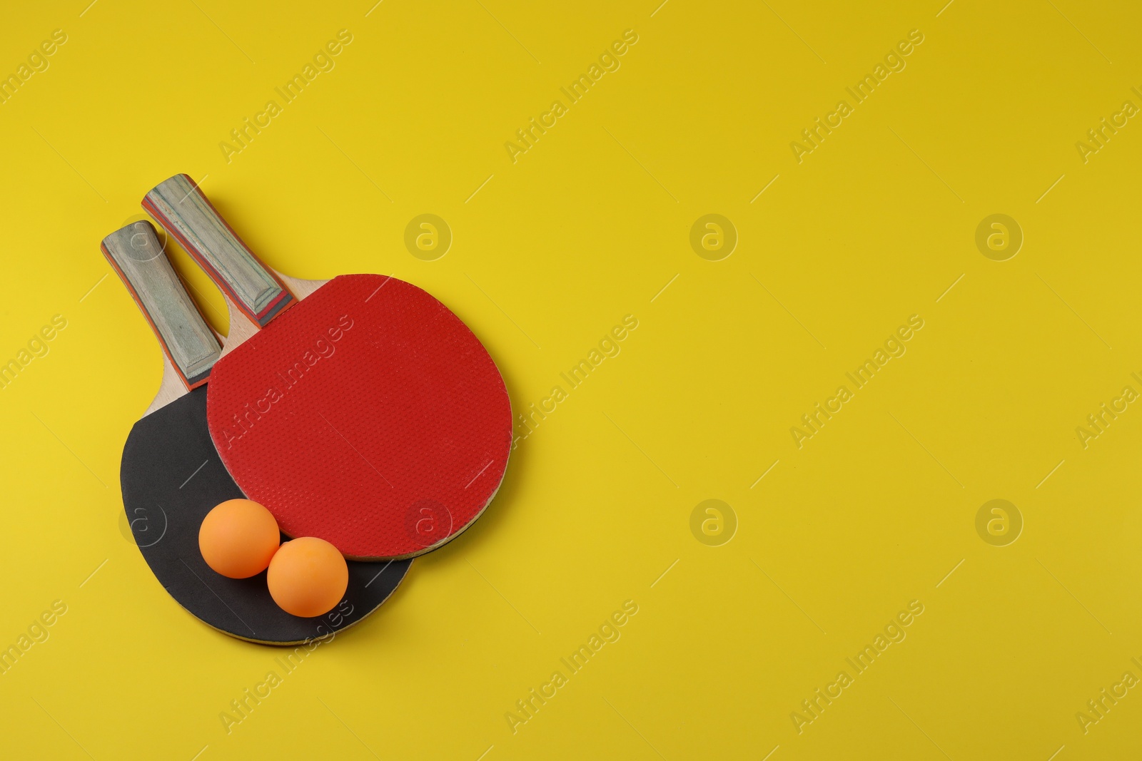 Photo of Ping pong balls and rackets on yellow background, flat lay. Space for text