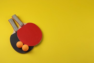 Photo of Ping pong balls and rackets on yellow background, flat lay. Space for text