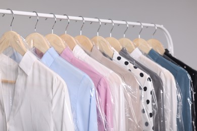 Photo of Dry-cleaning service. Many different clothes in plastic bags hanging on rack against grey background