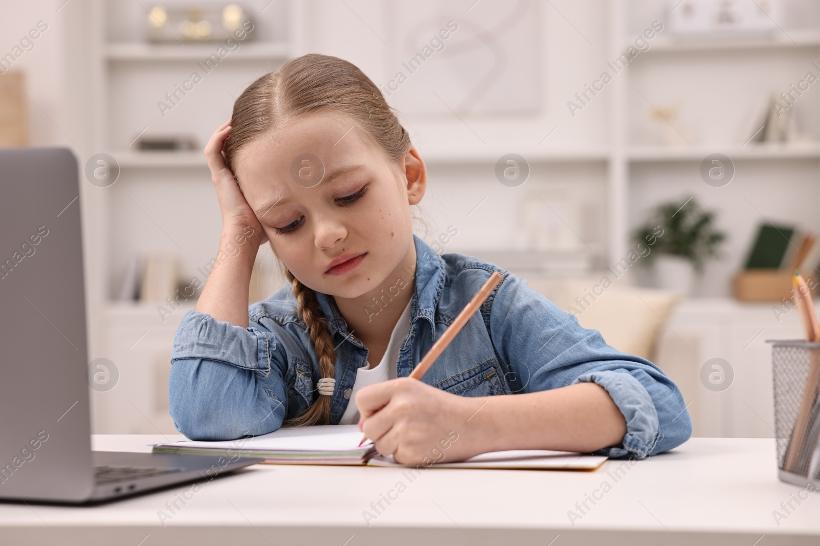 Photo of Little girl suffering from headache while doing homework at home