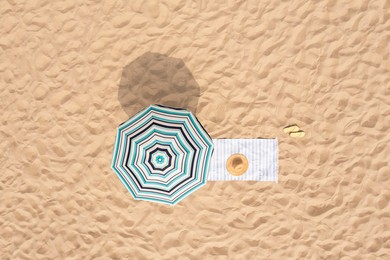 Beach umbrella near towel and other vacationist's stuff on sand, aerial view