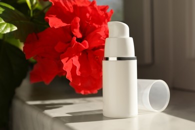 Bottle of face cream and flower on white table indoors
