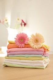 Stack of clean clothes and flowers on wooden table