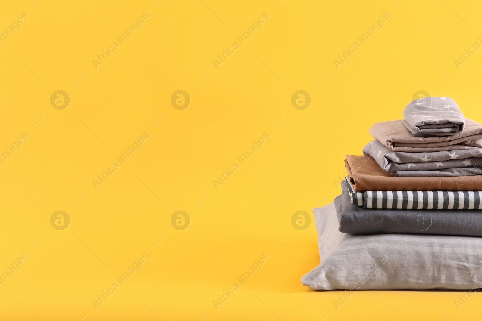 Photo of Stack of clean bed sheets and pillow on yellow background. Space for text