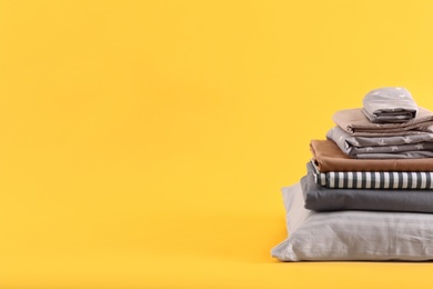 Stack of clean bed sheets and pillow on yellow background. Space for text