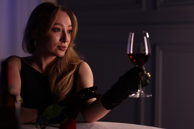 Photo of Elegant young woman with glass of wine at table indoors in evening