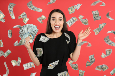 Happy young woman with dollars under money rain on red background