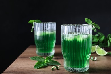 Photo of Delicious mint liqueur with green leaves and ice cubes on wooden table