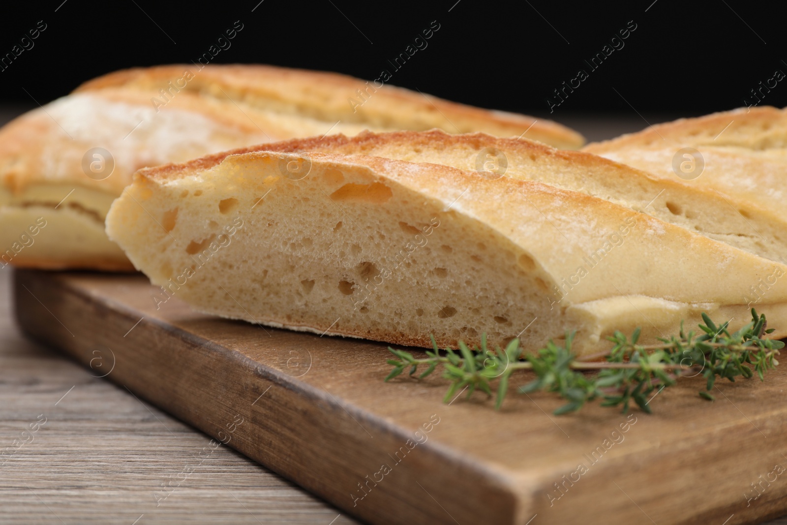 Photo of Cut tasty baguette with thyme on wooden table, closeup