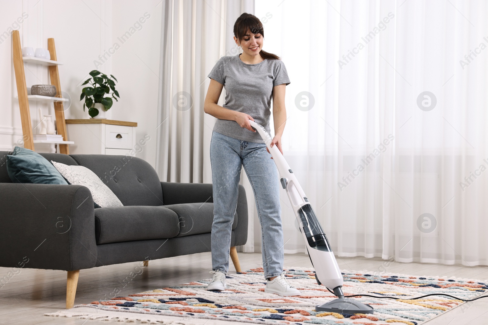 Photo of Happy young housewife vacuuming rug at home