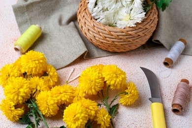Composition with knife, threads and Chrysanthemum flowers on light textured table