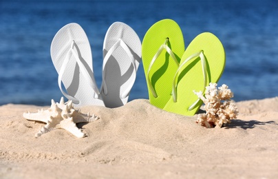 Photo of Composition with bright flip flops on sand near sea in summer. Beach accessories