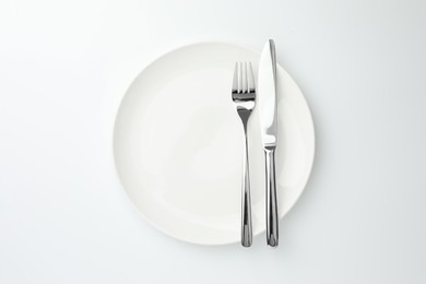 Plate, fork and knife on white background, top view