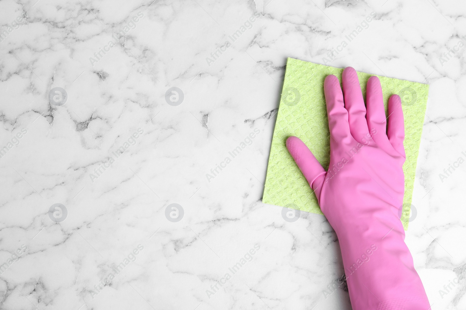 Photo of Woman in gloves wiping white marble table with rag, top view. Space for text