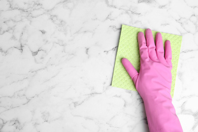 Photo of Woman in gloves wiping white marble table with rag, top view. Space for text