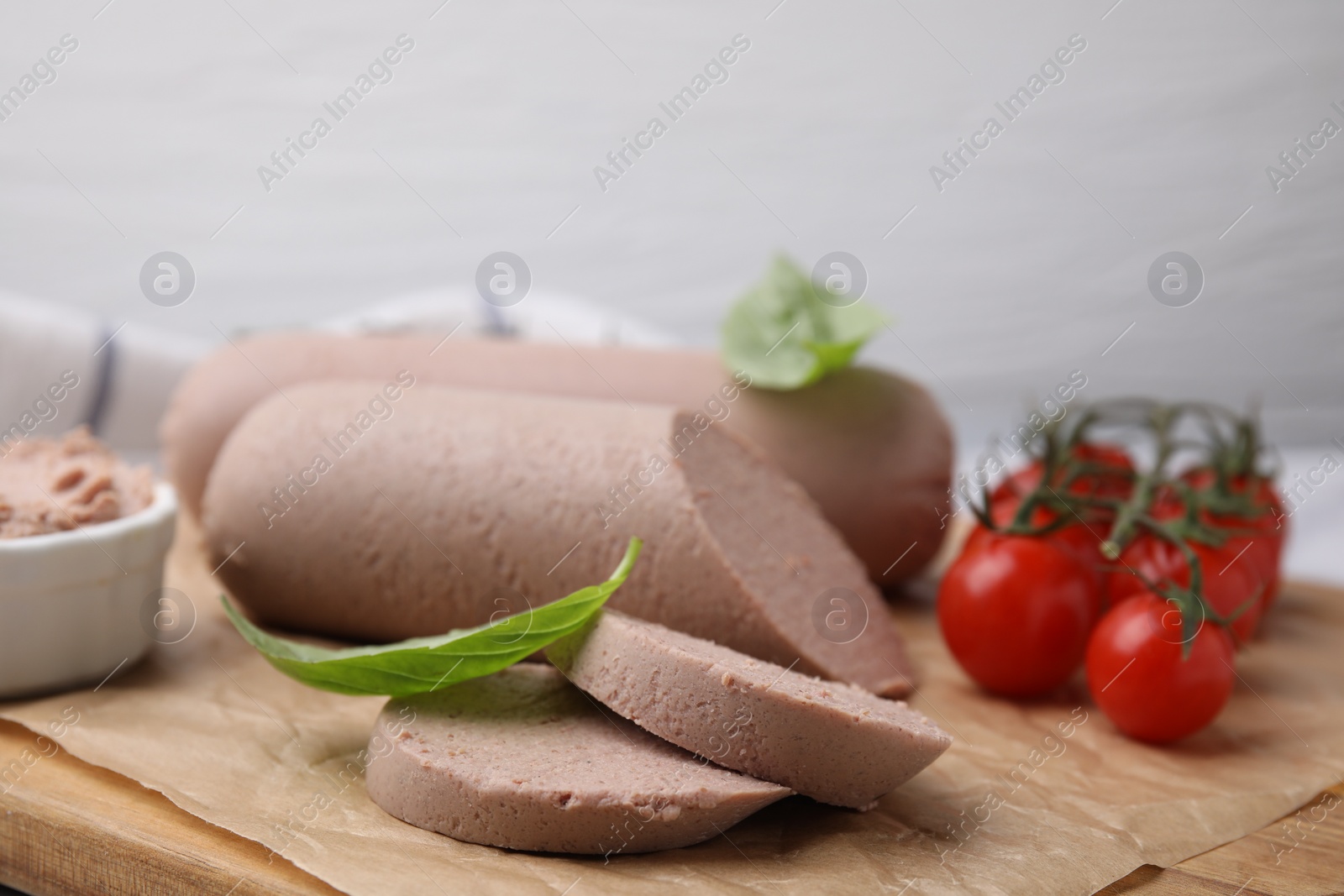 Photo of Delicious liver sausages and cherry tomatoes on wooden board, closeup