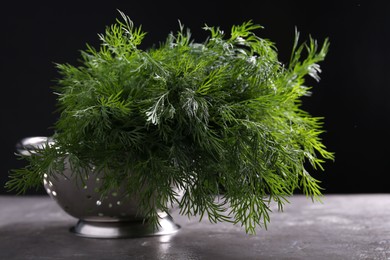 Photo of Fresh wet dill in colander on grey textured table against black background, closeup