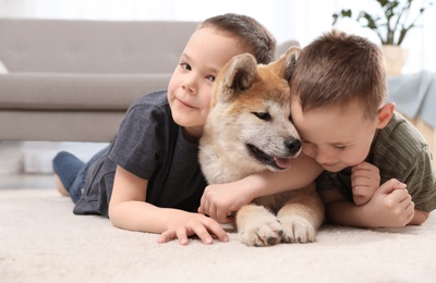 Happy boys with Akita Inu dog on floor in living room. Little friends