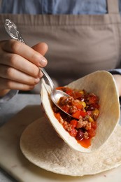 Photo of Woman putting tasty chili con carne into tortilla at white table, closeup