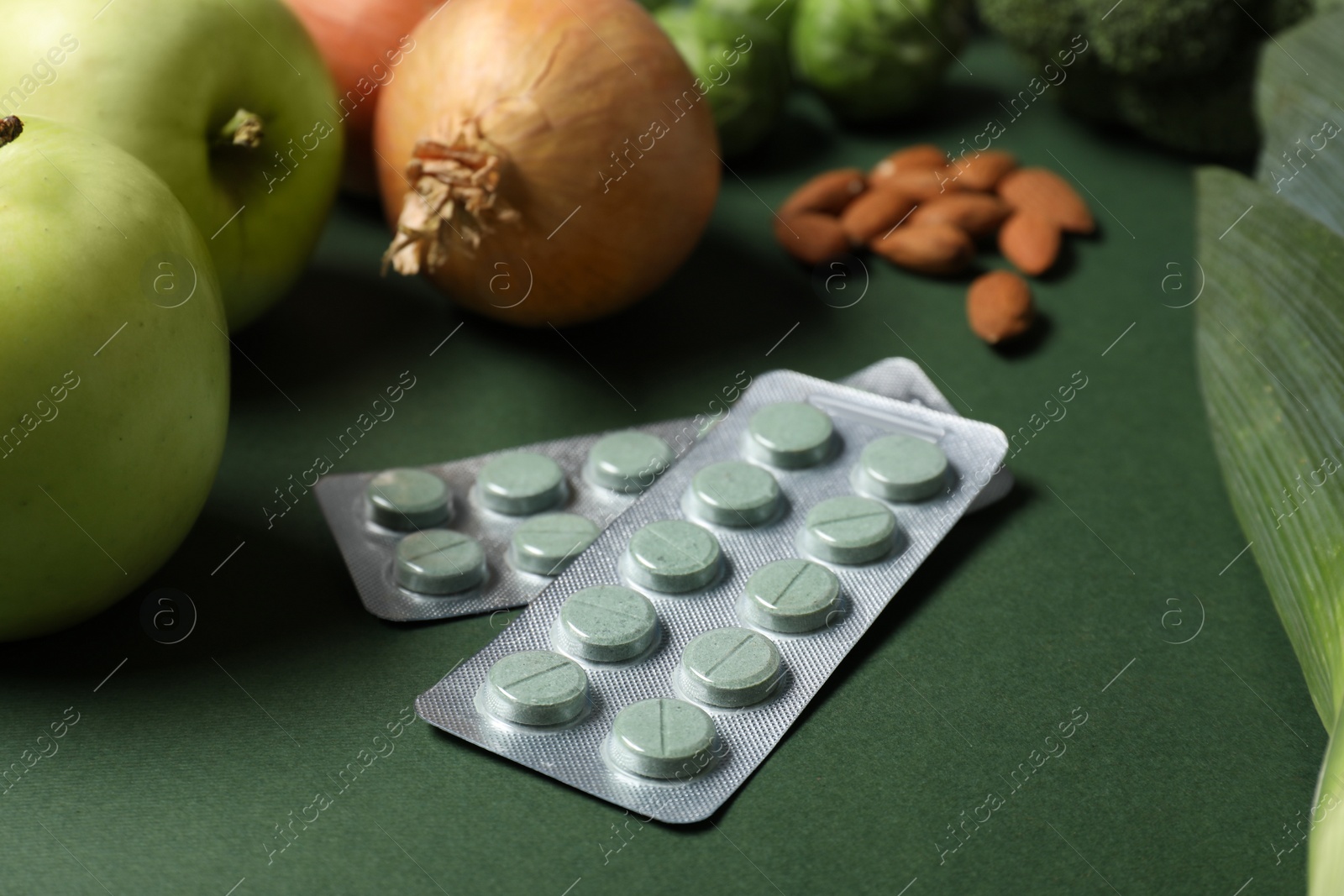 Photo of Blisters with pills and food on green background, closeup. Prebiotic supplements