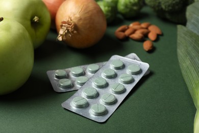 Photo of Blisters with pills and food on green background, closeup. Prebiotic supplements