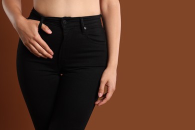 Photo of Woman wearing stylish black jeans on brown background, closeup. Space for text