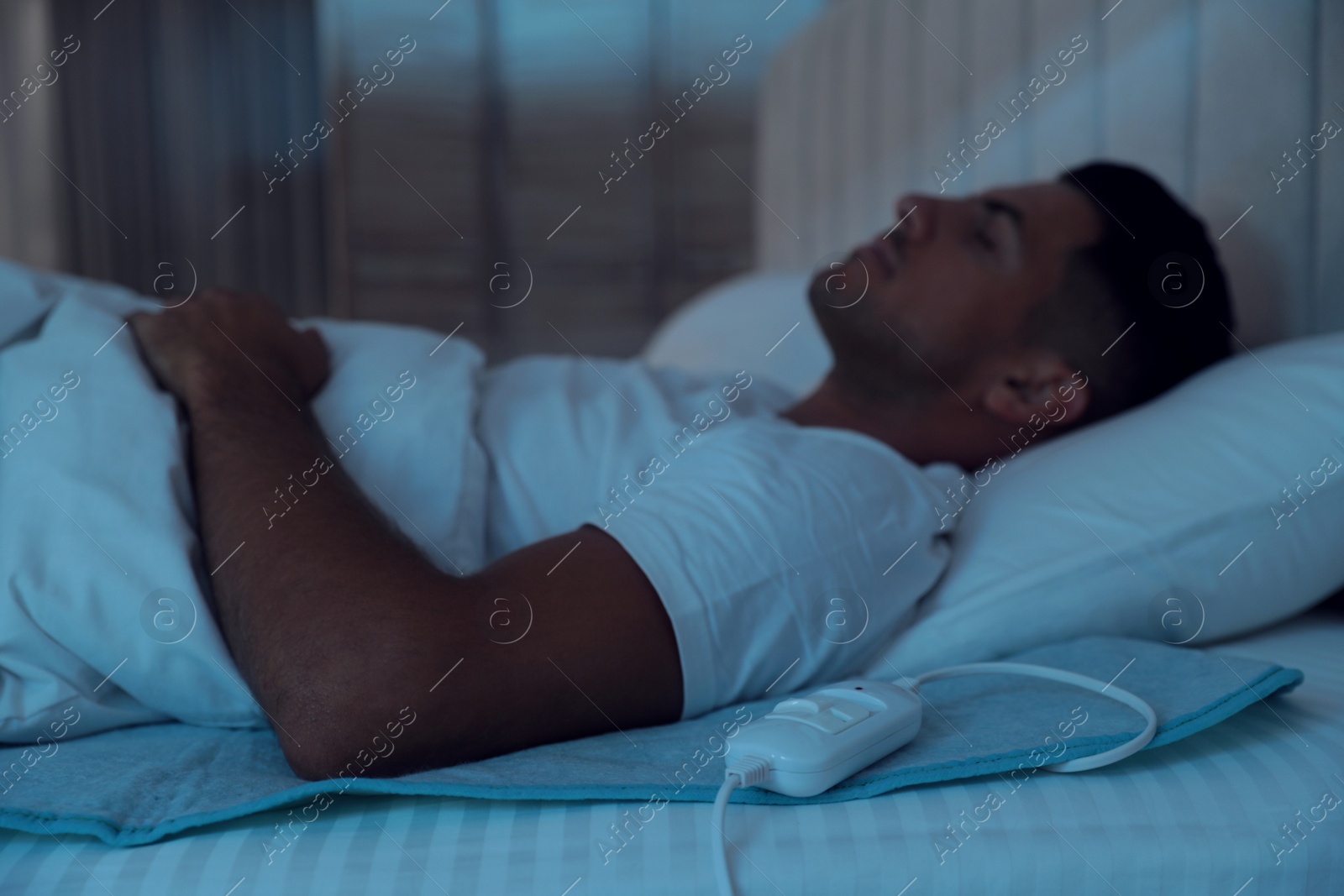 Photo of Man sleeping in bed with electric heating pad, focus on cable