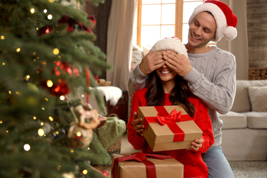 Photo of Happy couple with gift boxes in living room decorated for Christmas