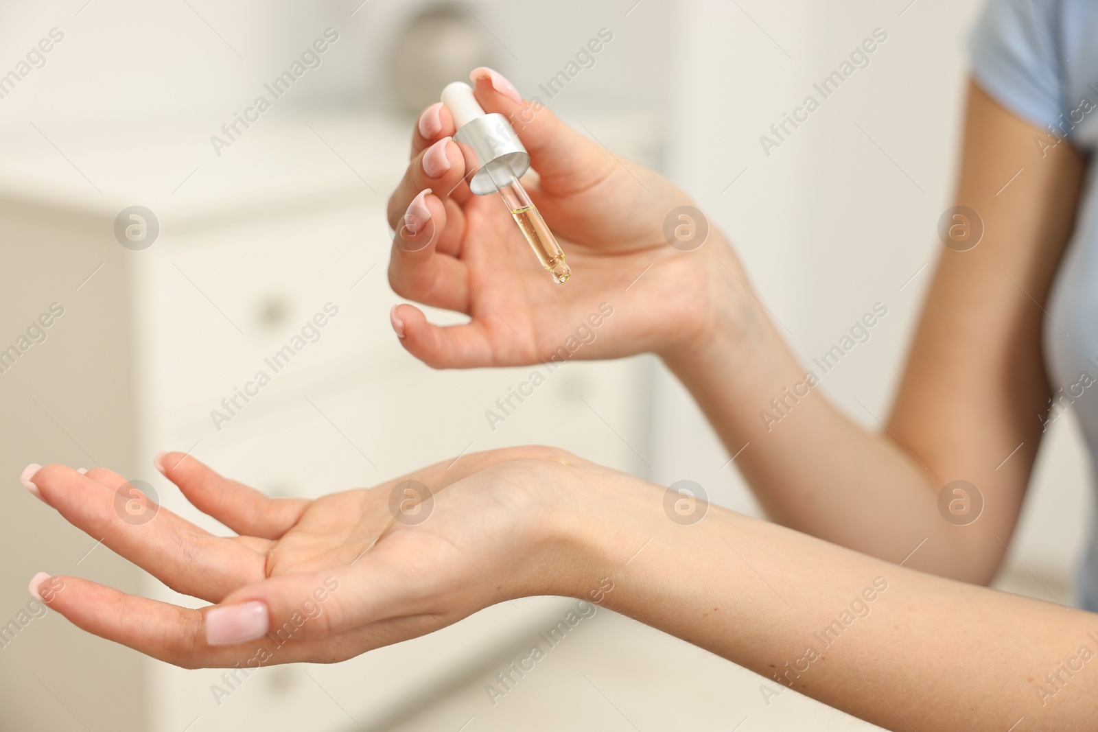 Photo of Aromatherapy. Woman applying essential oil onto wrist against light background, closeup