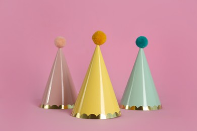 Colorful party hats with fluffy balls on pink background