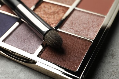Beautiful eye shadow palette and brush on grey table, closeup
