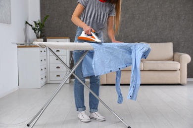 Photo of Young woman ironing clothes on board at home, closeup