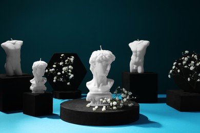 Photo of Stylish presentation of sculptural body candles and gypsophila flowers on light blue table