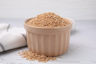 Dry wheat groats in bowl on white textured table, closeup