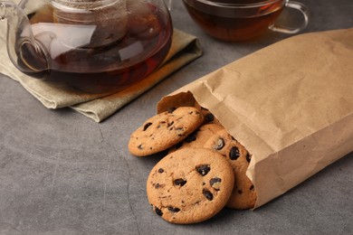 Photo of Paper bag with delicious chocolate chip cookies and tea on grey table, closeup. Space for text