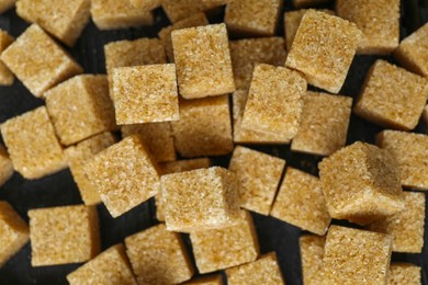 Photo of Brown sugar cubes on dark table, top view