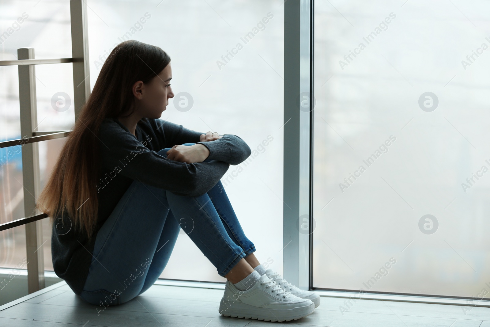 Photo of Upset teenage girl sitting at window indoors. Space for text