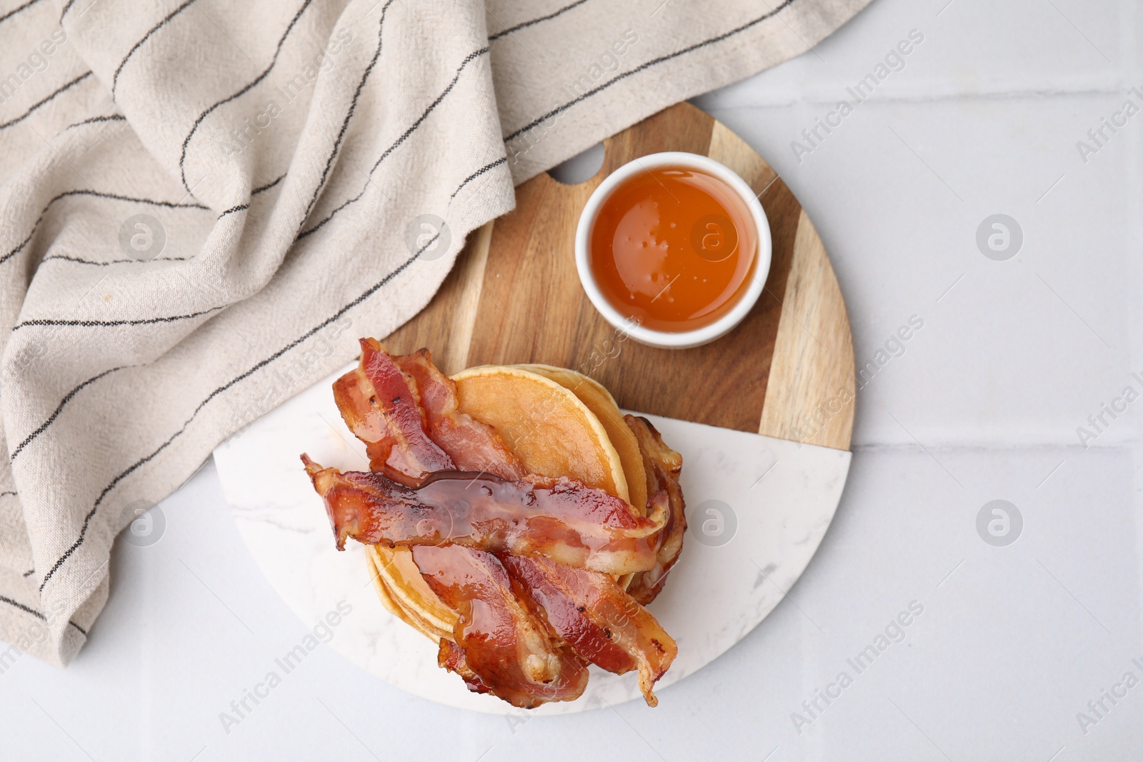 Photo of Delicious pancakes with bacon and honey on white tiled table, top view