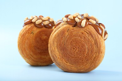 Photo of Supreme croissants with chocolate paste and nuts on light blue background, closeup. Tasty puff pastry