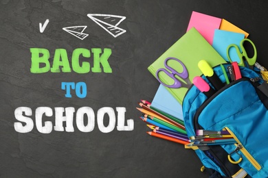 Image of Text Back To School and backpack with different stationery on black chalkboard, top view