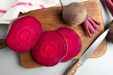 Photo of Cut raw beet and knife on light grey table, flat lay