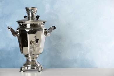 Photo of Metal samovar on grey table against light blue background, space for text. Russian tea culture