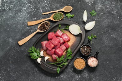 Photo of Raw beef meat and different ingredients for cooking delicious goulash on black textured table, flat lay