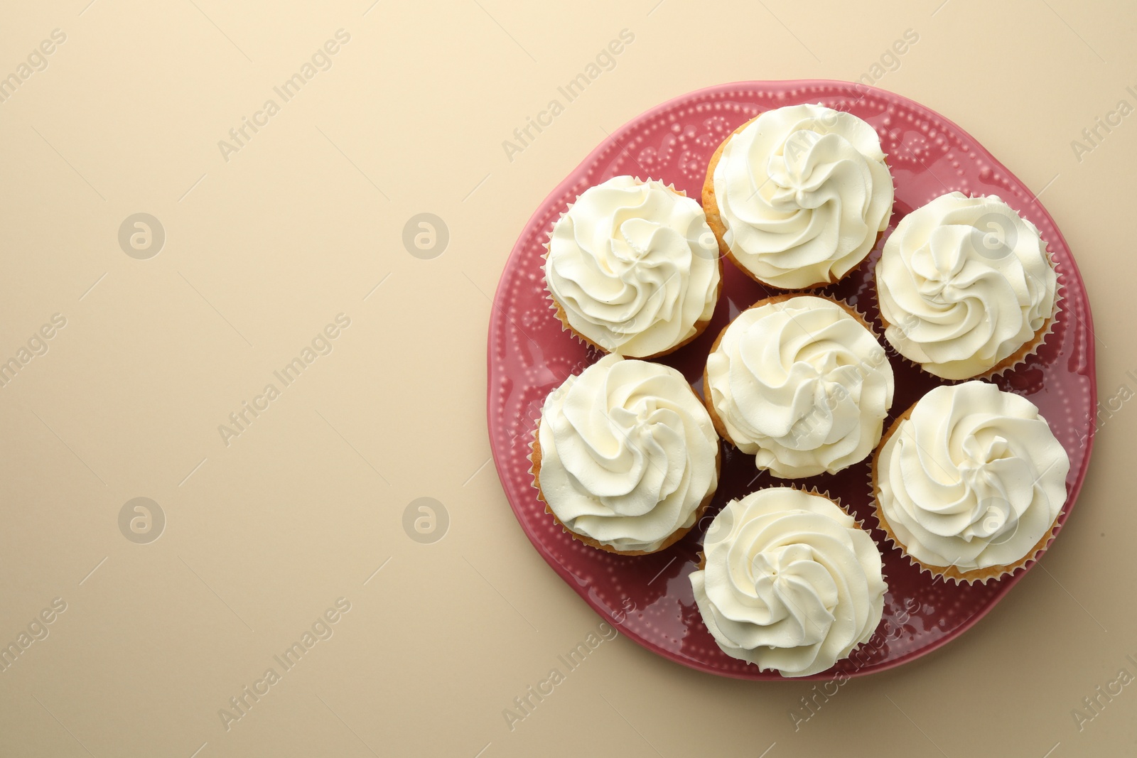 Photo of Tasty vanilla cupcakes with cream on beige background, top view. Space for text