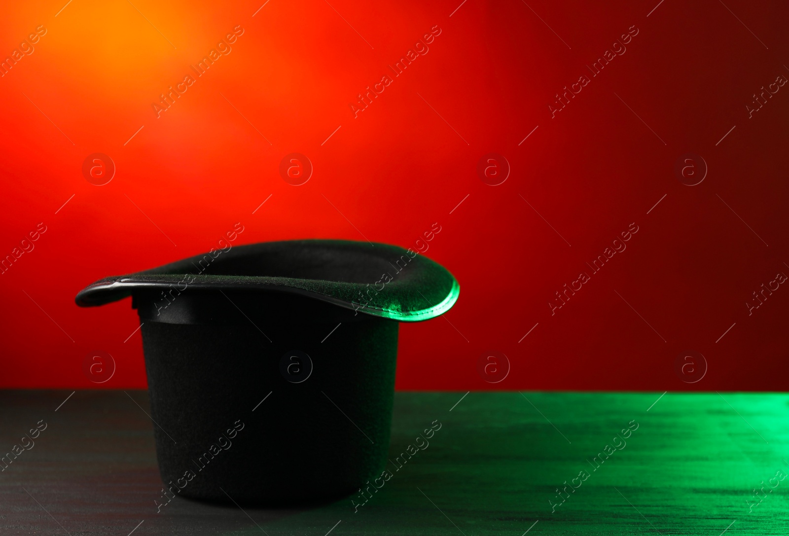 Photo of Magician's hat on black wooden table against color background, space for text