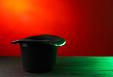 Photo of Magician's hat on black wooden table against color background, space for text