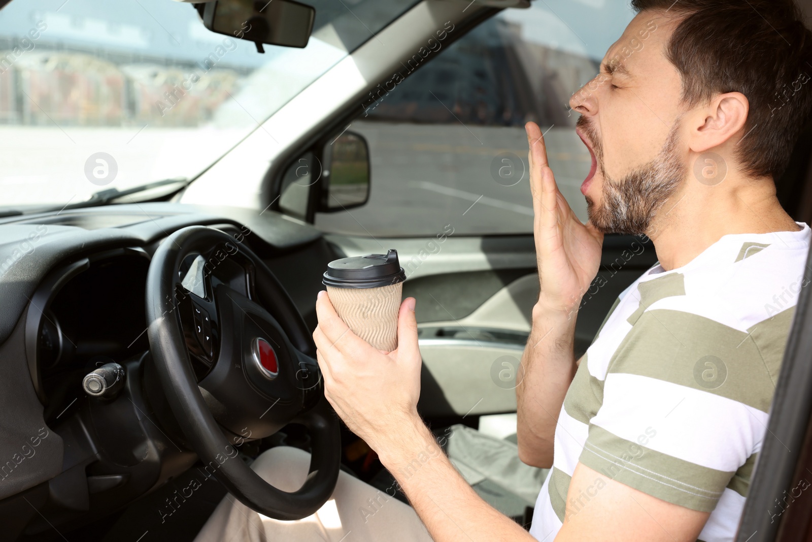 Photo of Sleepy man with cup of coffee yawning in modern car