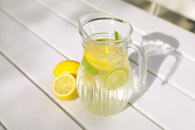 Jug of water with lemons and mint on white wooden table outdoors