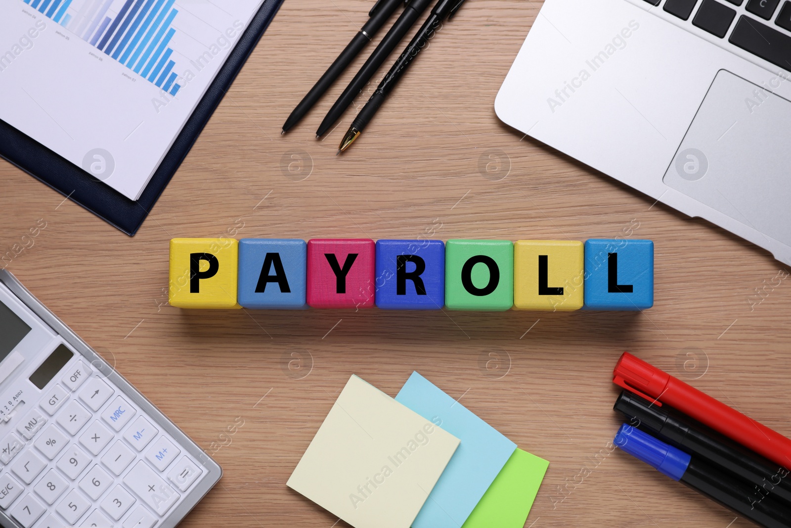 Photo of Colorful cubes with word Payroll, laptop and stationery on wooden table, flat lay
